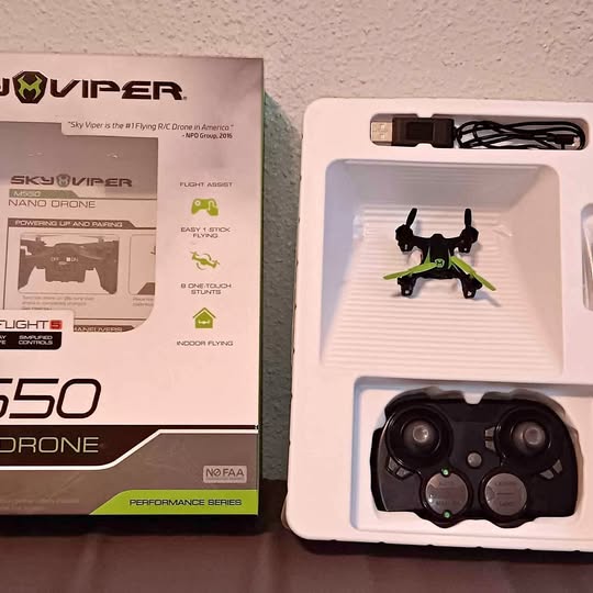 Nano drone with green arms in retail box, camera module visible