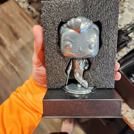 Diecast toy figure with blue-gray head, orange markings, standing on round base