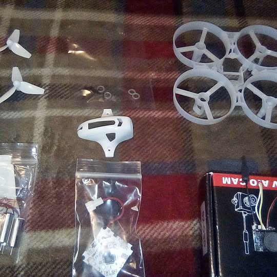 DIY tinywhoop drone kit with white frame, propellers, controller, and spare parts bags