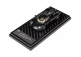 Black diecast sports car model with carbon-fiber base, 1:64 scale, front three-quarter view
