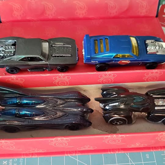 Set of four Hot Wheels diecast cars in black, gray, blue, and dark multi-color.
