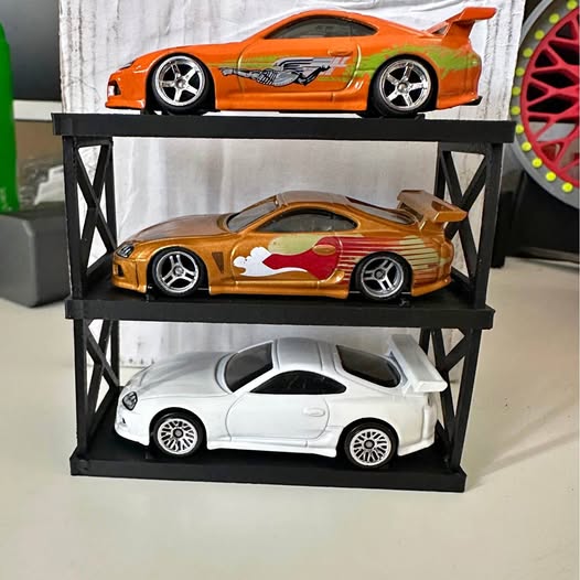 Diecast car display stand with three model cars: orange, gold, and white