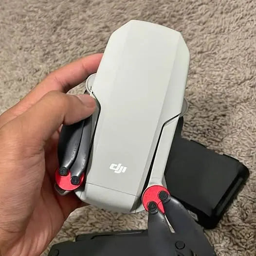 White DJI mini drone with red accents, held in hand; visible DJI logo