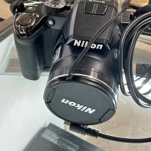 Nikon P100 camera with lens cap and side controls, with attached cable