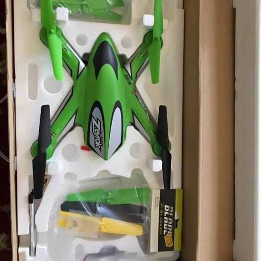 Green and black quadcopter drone in a white box insert, with four propellers