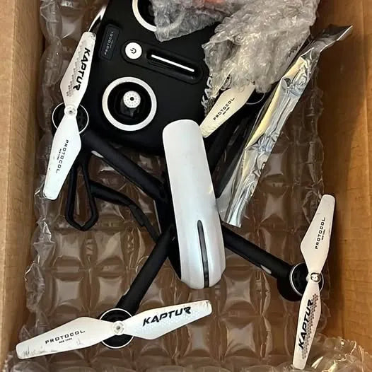 Black drone with white propellers and arms, partially visible in packaging.
