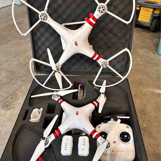 White quadcopter drone with red stripe arms and camera, stored in open case