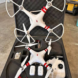 White quadcopter drone with red stripe arms and camera, stored in open case