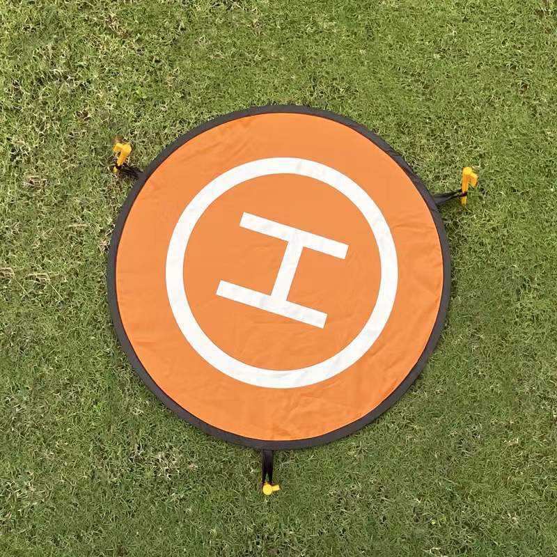 Round orange drone landing pad with white circle and E symbol, black edge, corner stakes