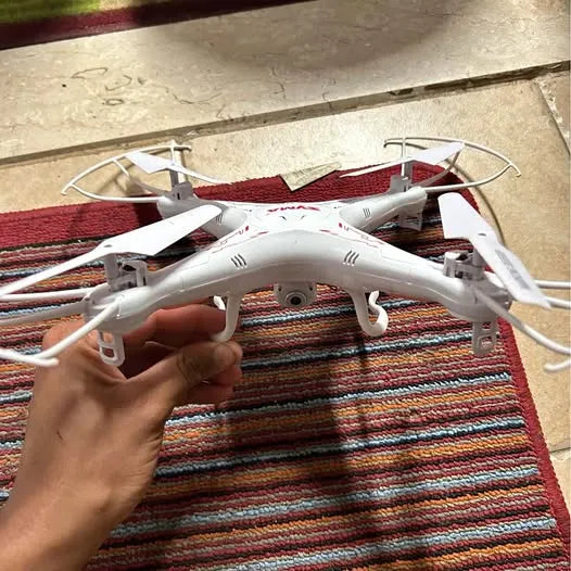 White quadcopter drone with propellers and landing gear, held in hand
