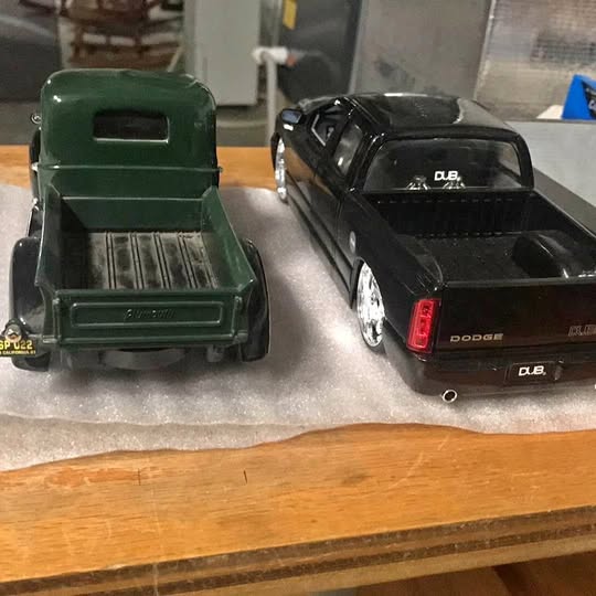 Diecast 1/24 scale trucks: green open-bed truck and black D.B. pickup on display