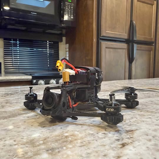 DJI FPV quadcopter drone with black frame, orange wires, exposed front camera