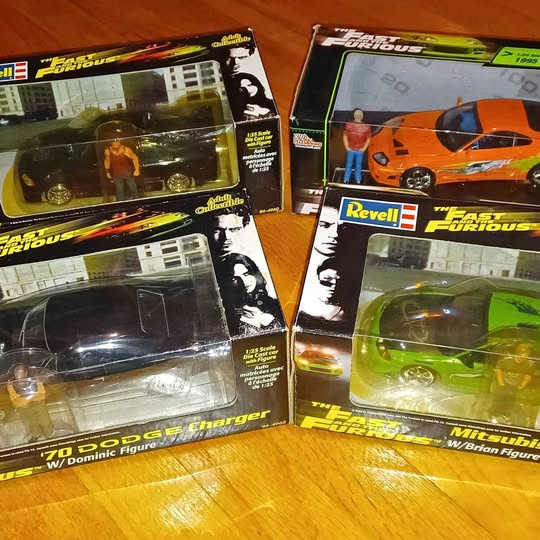 Diecast car figures in retail boxes, featuring an orange car and a green car