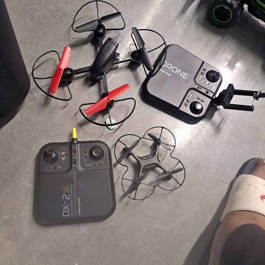 Quadcopter drone set with dark gray controller and two drones with red prop blades