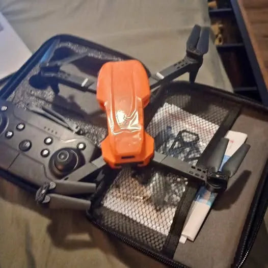 Orange quadcopter drone with camera, landing legs and propellers attached.