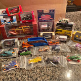 Diecast toy lot with assorted miniature cars, trucks, and racing vehicles in boxes