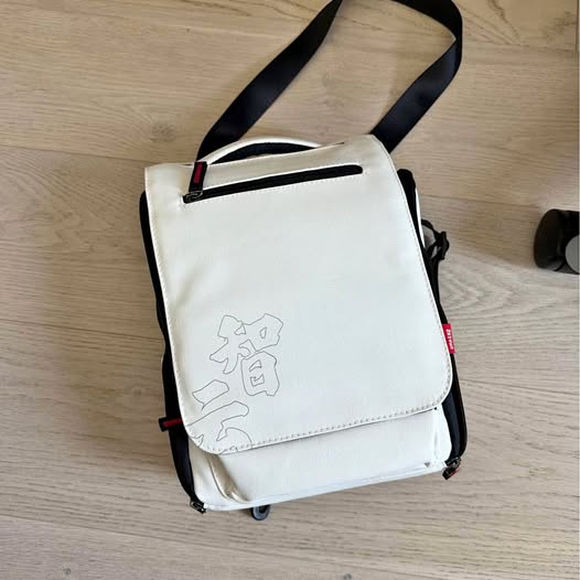 White camera accessory shoulder bag with adjustable strap and logo patch