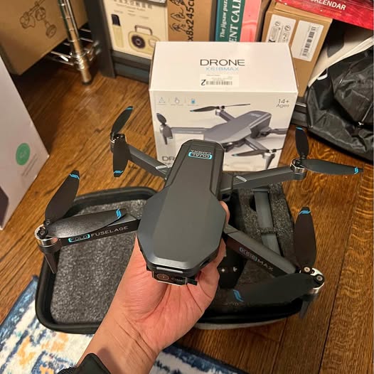 Gray quadcopter drone with camera, held in hand, visible front and landing gear