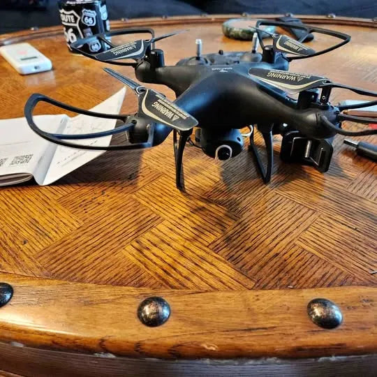 Black quadcopter drone with four rotors and front camera, resting on a surface