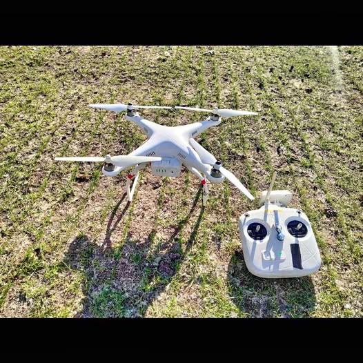 White quadcopter drone with four rotors and handheld remote controller