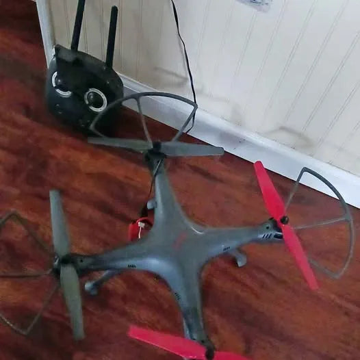 Gray quadcopter drone with four propellers and red blade guards.