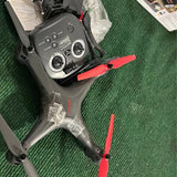 Gray drone controller with red joysticks and visible red propeller blades