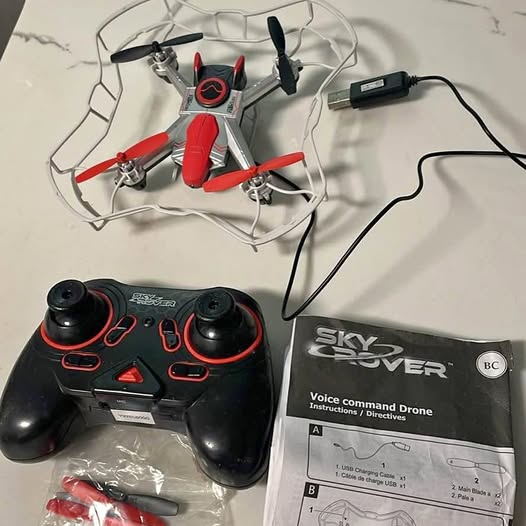 Red and gray quadcopter drone with propellers and black voice-command remote controller