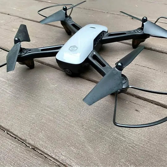 White quadcopter drone with four gray propellers and black arms, with connected cable