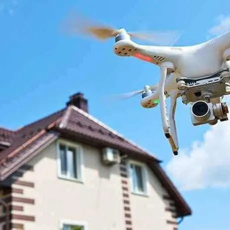 Real estate drone with camera hovering near house roof.
