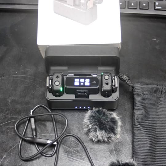 Wireless microphone transmitters in open charge case, with display screen and windscreen