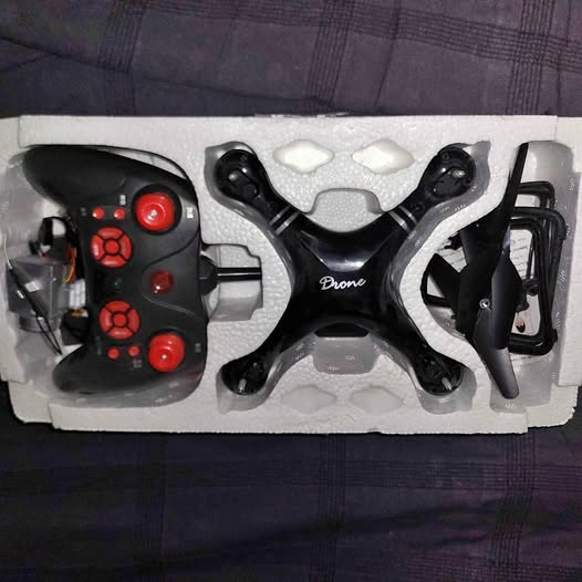 Black quadcopter drone with red LEDs and remote controller, in protective foam tray
