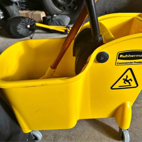 Yellow janitor mop bucket with wheels and handle, with safety warning label