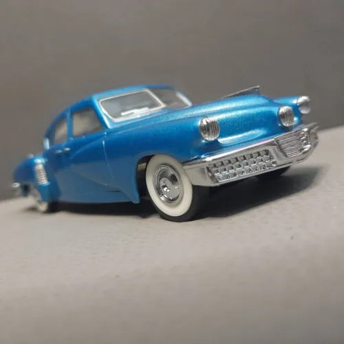 Blue diecast model car with chrome grille, front bumper, and whitewall-style tires