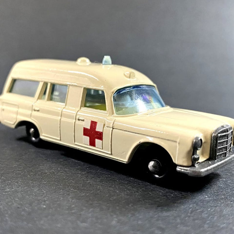Cream diecast ambulance van with red cross on side, detailed grille and windows.