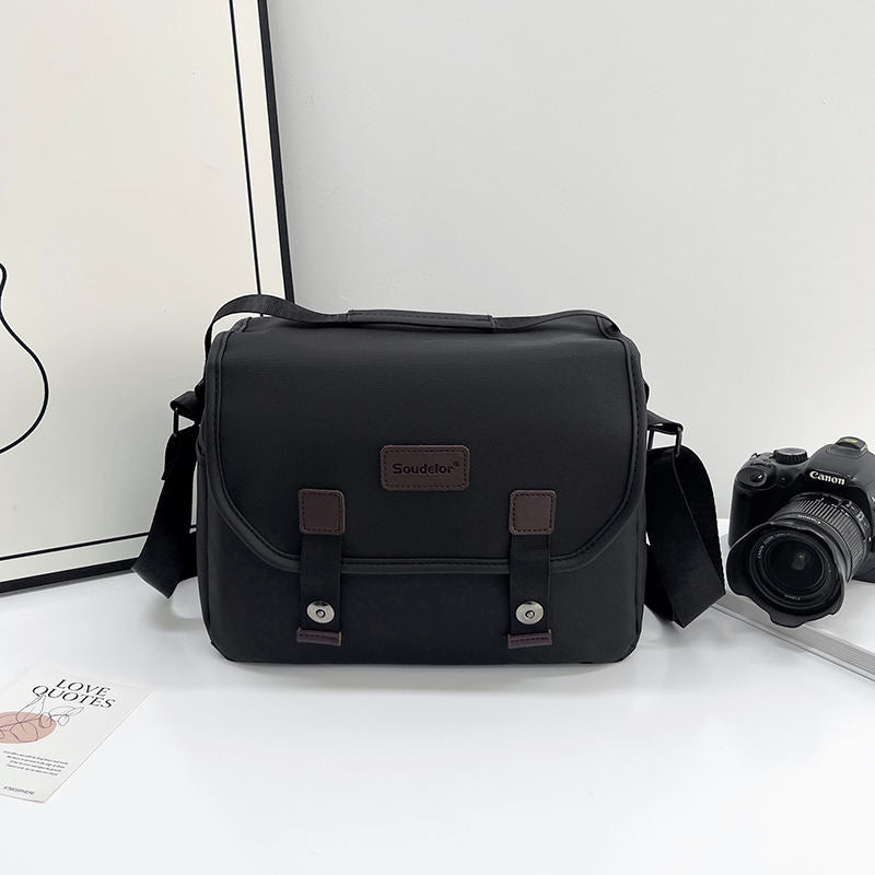 Black camera travel shoulder bag with front flap and dual buckles
