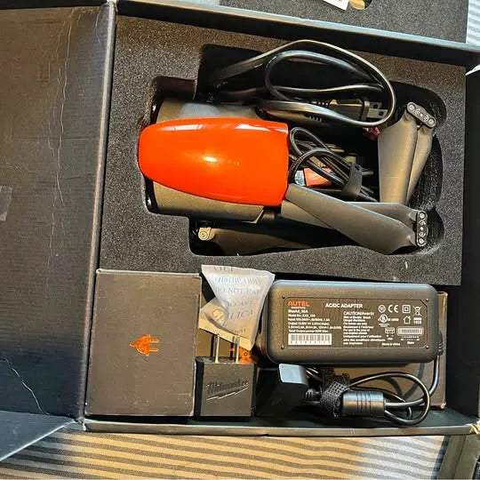 Orange and gray drone with arms, plus attached battery and cables in packaging