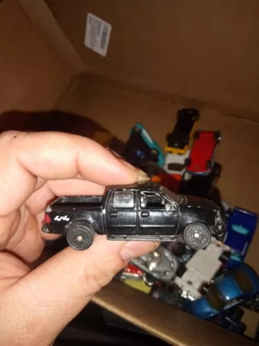 Black diecast pickup truck model with side view, held in hand, 1/64 scale.