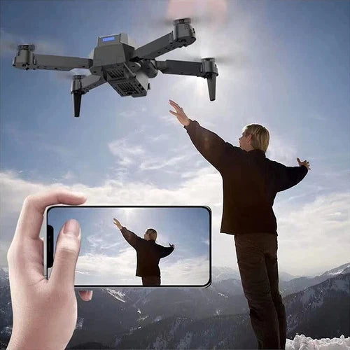 Foldable quadcopter drone with front camera, hovering; smartphone screen shows live view.