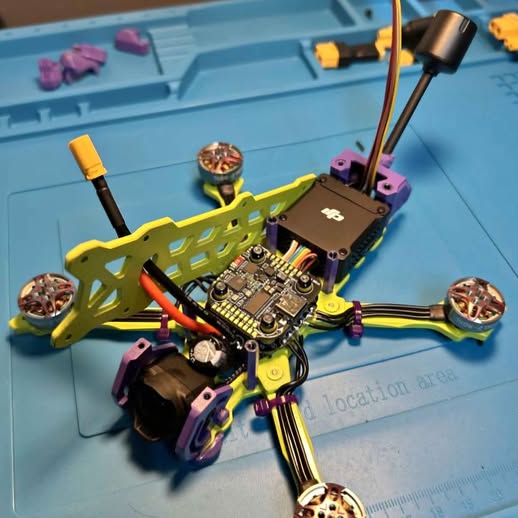 FPV racing drone with yellow frame, electronic circuit board, and four prop arms