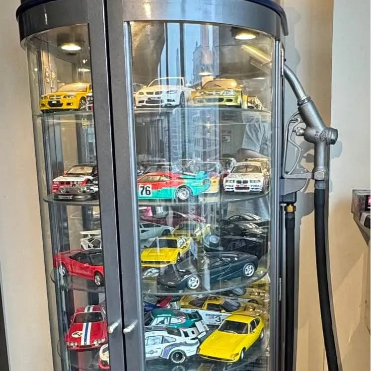 Glass display cabinet with assorted diecast cars, viewed through curved front door