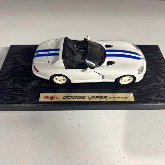 Diecast sports car with white body and blue racing stripes, black hood, on display base.