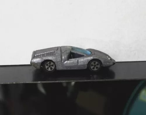 Die-cast toy car with metallic gray body and blue windows, on a black base
