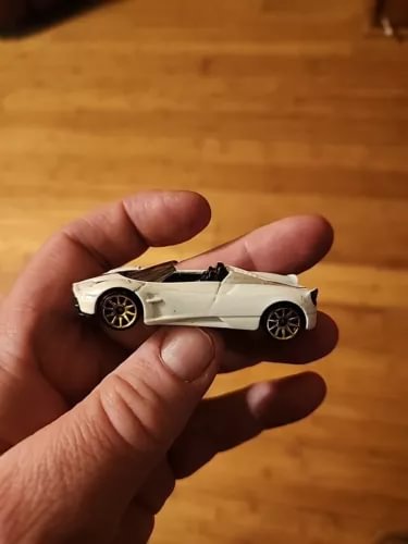 White 1/64 diecast roadster car with black wheels, side view in hand