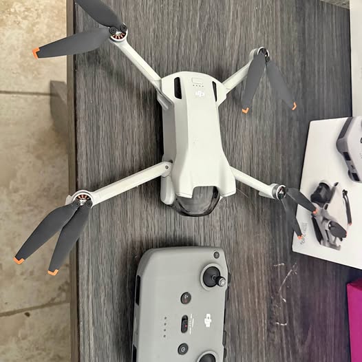 White quadcopter drone with four propellers and front camera gimbal, plus remote controller