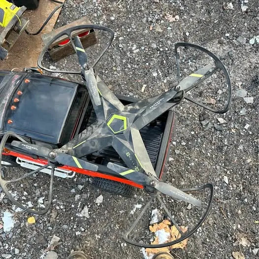 Quadcopter drone with four gray arms, green accents, and blue display screen