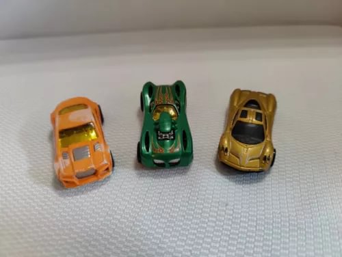Three diecast toy cars: orange, green, and gold with detailed wheels and windows