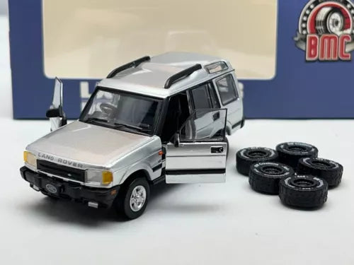Silver diecast SUV model with black roof and open door, plus five spare tires