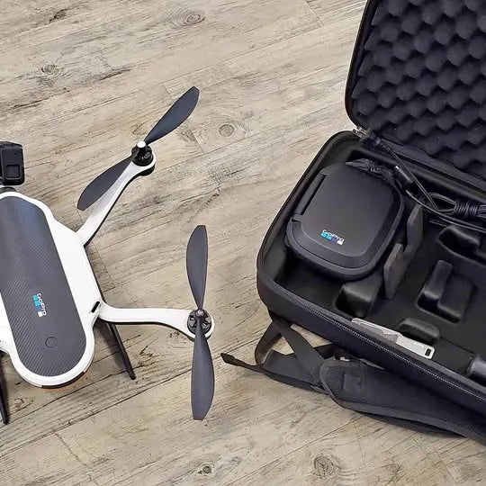 White quadcopter drone with three-blade propellers beside a padded hard case