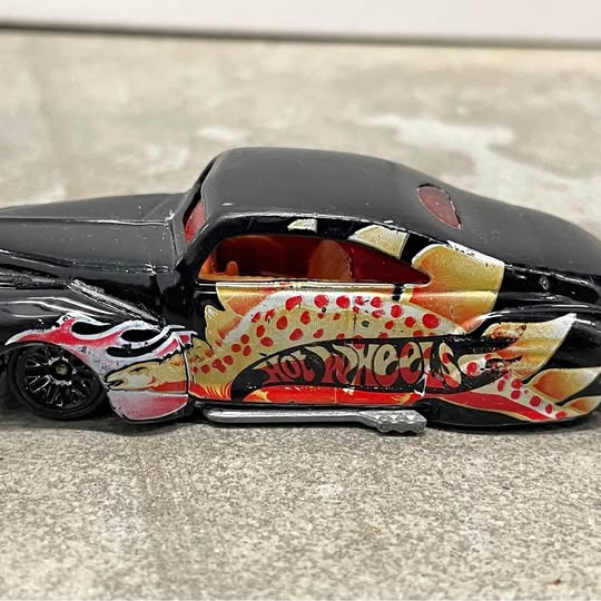 Die-cast hot rod toy in black with flame graphics and Hot Wheels logo, side view.