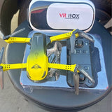 Yellow quadcopter drone with four rotors, shown with VR headset in packaging